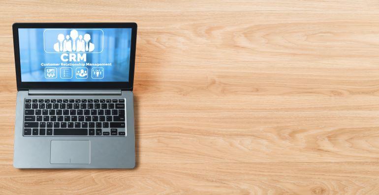 Laptop with CRM illustration on screen, on wooden surface