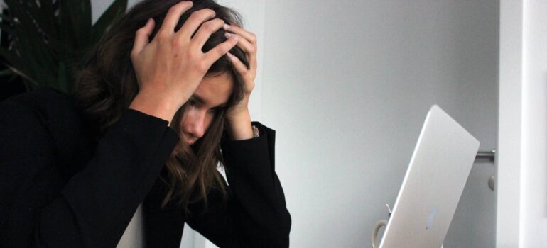 A person holding their head in front of a laptop screen.