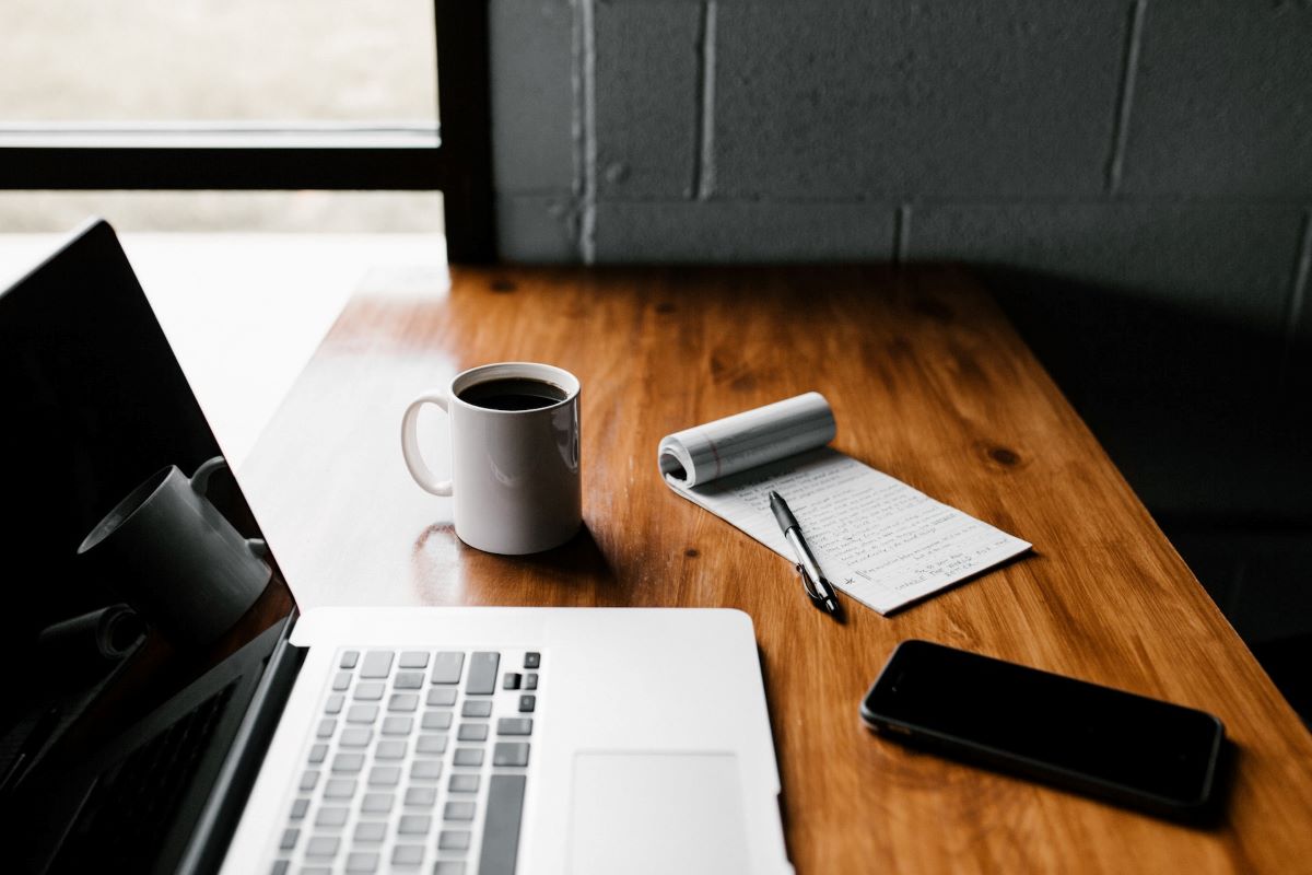 Laptop, coffee mug, notepad, and smartphone on table | The importance of nurturing a blog for your business